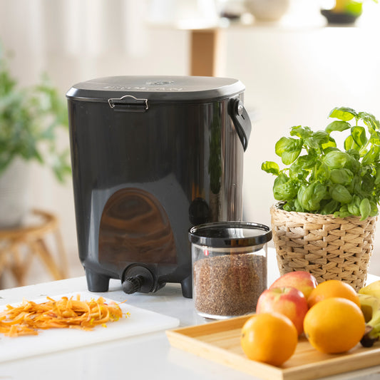 Black Bokashi composter on a counter with fruits and vegetables