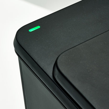 Close-up of a black toilet with a green indicator light on a white background